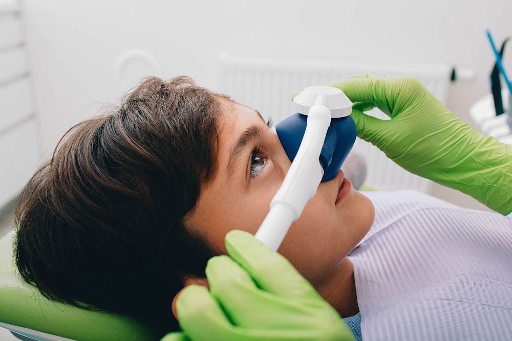 Boy receiving dental care with a gas mask, dentist's gloved hands near face.